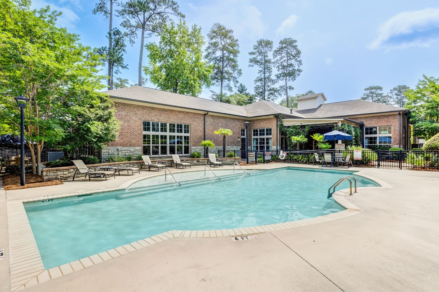 Pool area with brick building, chairs, and clear water, sunny day at Arcadia's Edge in Columbia, SC.