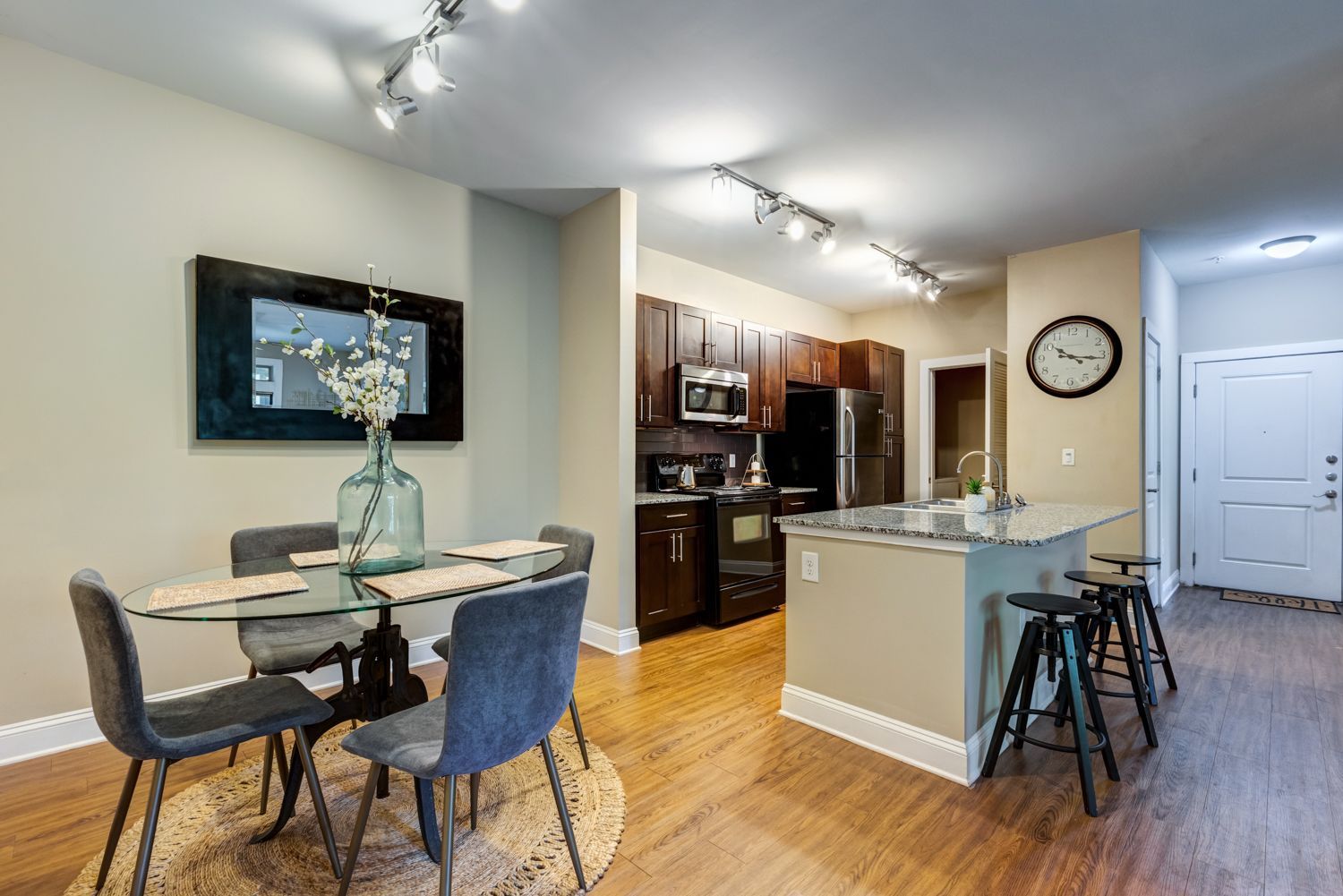 A modern kitchen and dining area. Glass table with grey chairs, dark cabinets, and a breakfast bar with stools at Arcadia's Edge in Columbia, SC.
