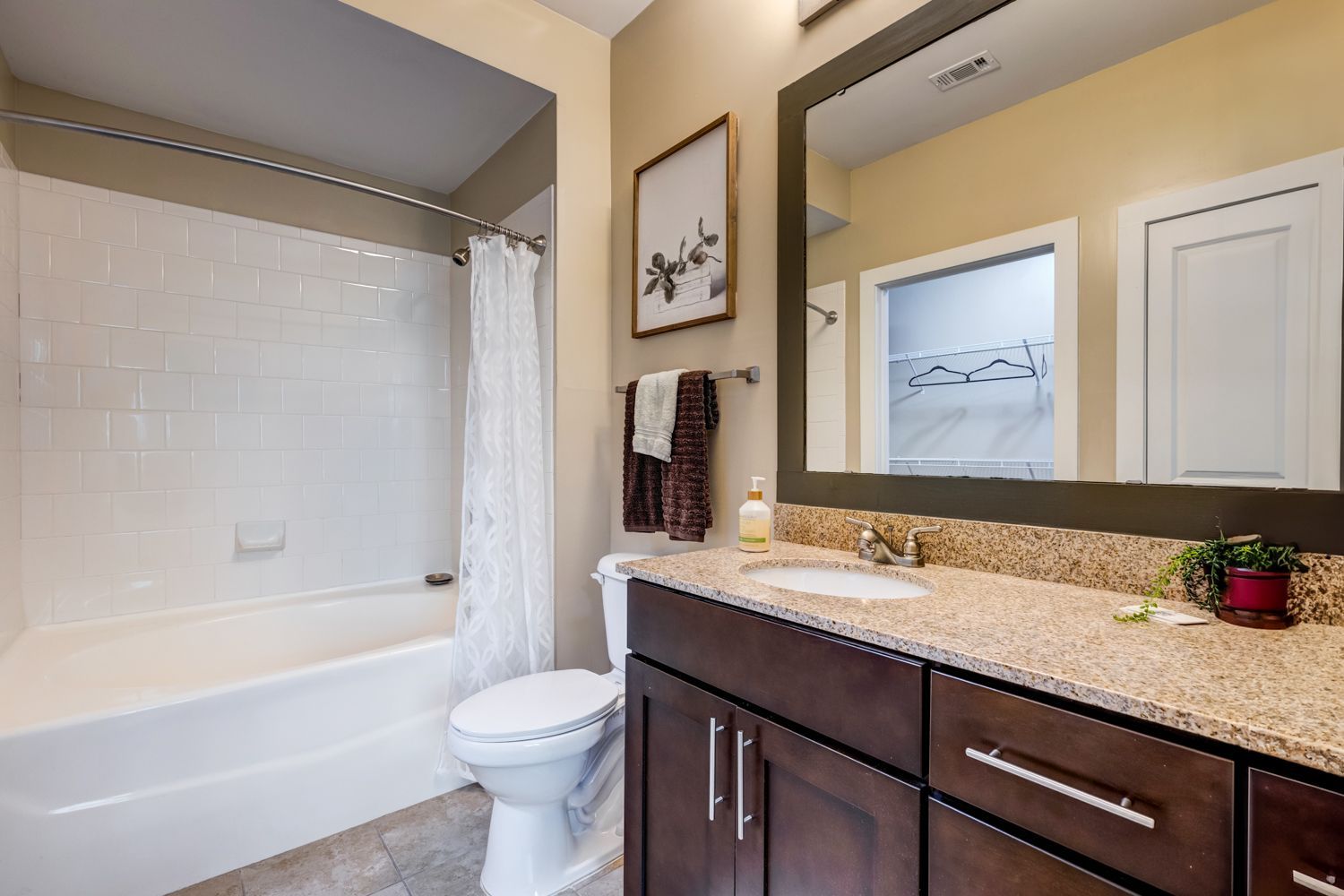 Bathroom with white tub, toilet, dark brown cabinets, tan countertop, and a large mirror at Arcadia's Edge in Columbia, SC.