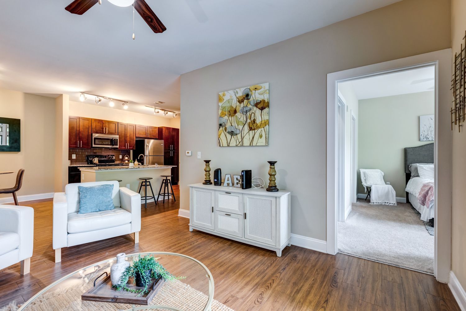 Living room with a view of the kitchen and bedroom; white chairs, wood floors, neutral walls, modern décor at Arcadia's Edge in Columbia, SC.