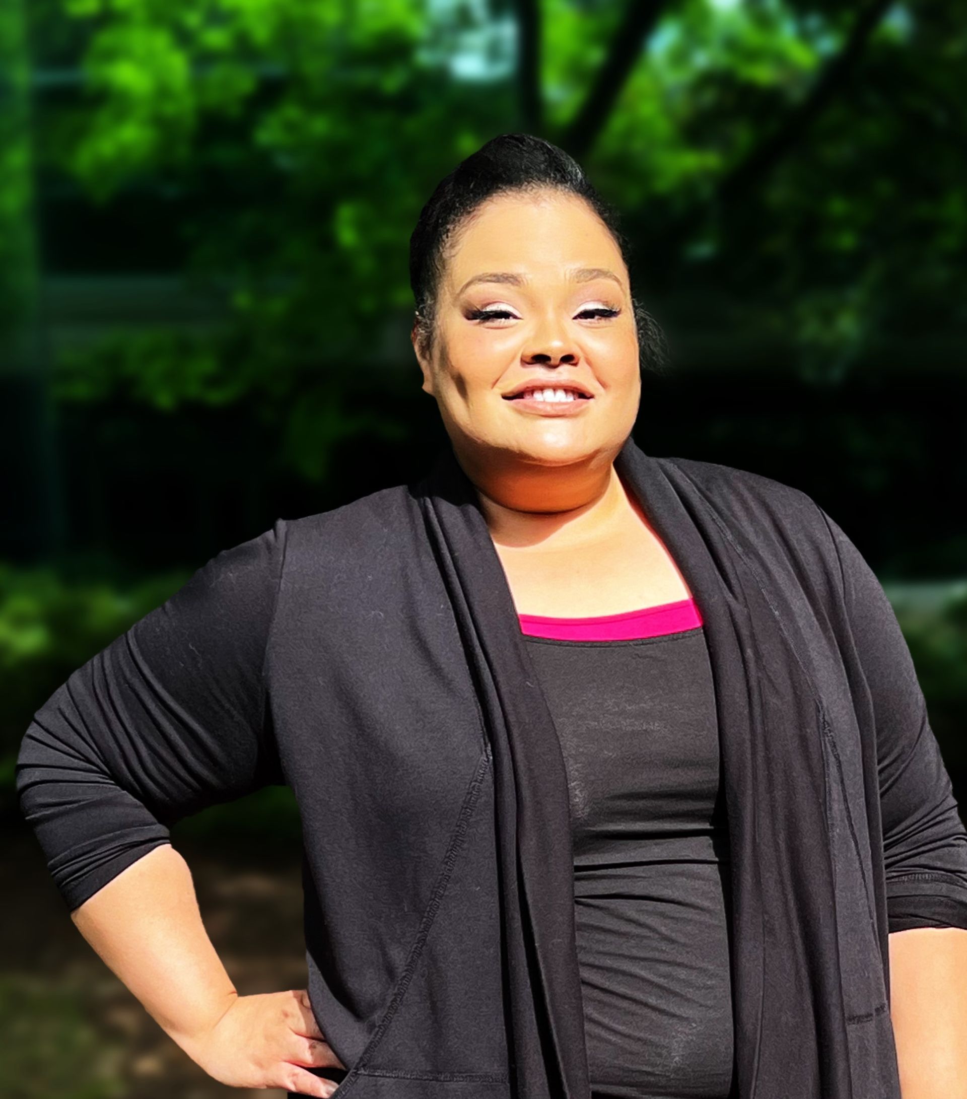 A woman wearing a black cardigan and a pink top is standing with her hands on her hips.