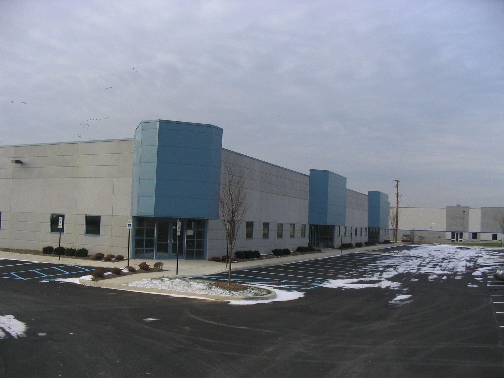 A curved, translucent panel canopy supported by a red steel frame, adjacent to a building with red grid window frames.