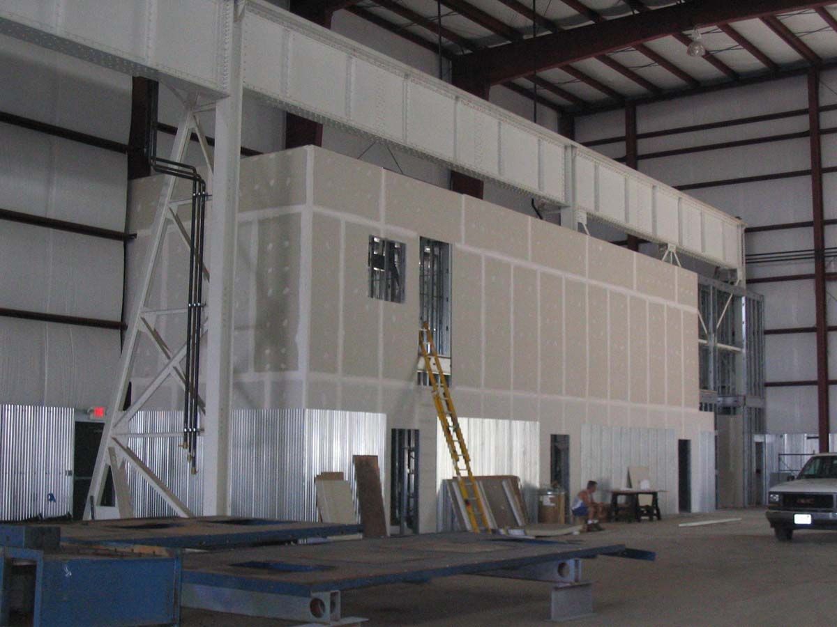 Interior of a large warehouse with an unfinished, two-story wall construction project featuring a yellow ladder.