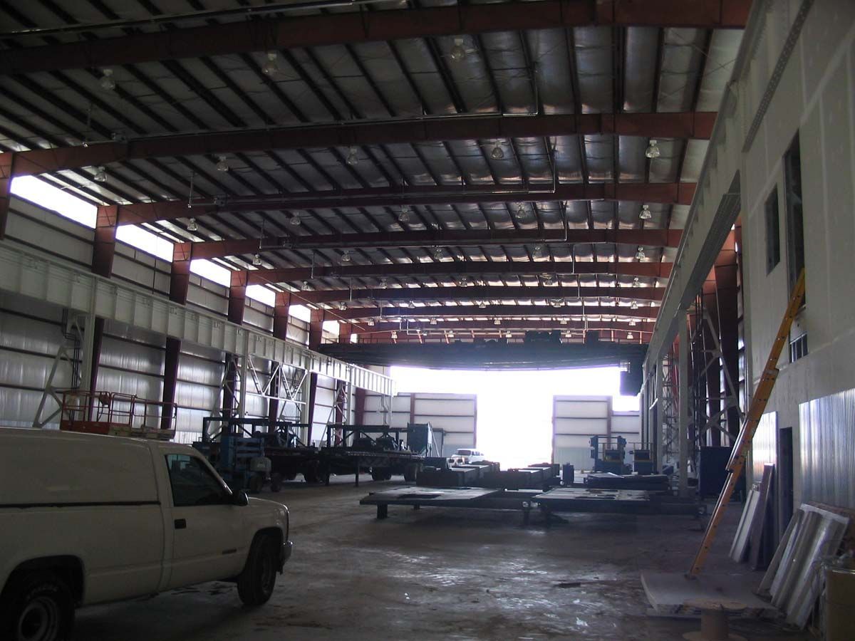 Interior of a large industrial warehouse with a white utility truck parked on the left and equipment scattered throughout.