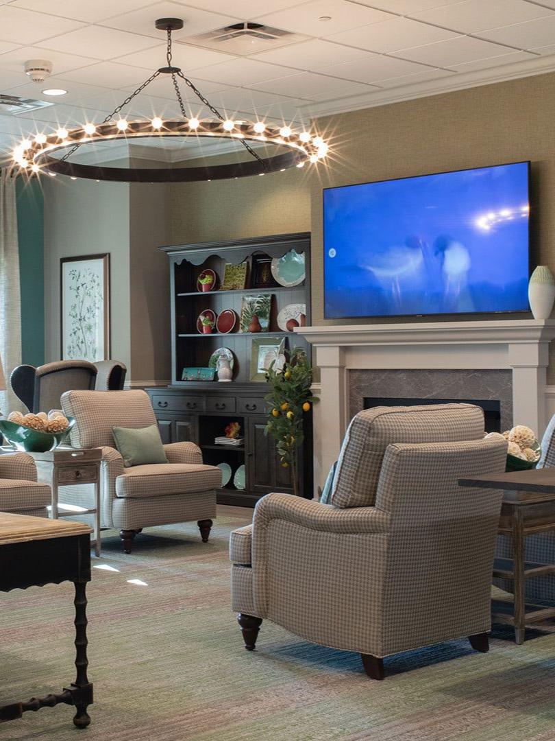 A cozy sitting area featuring two upholstered armchairs, a fireplace with a large wall-mounted TV, and a circular chandelier.