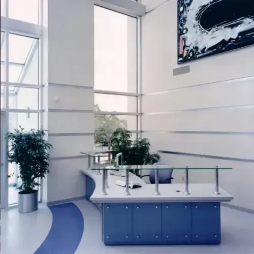 A modern reception area with a curved blue desk, floor-to-ceiling windows, green plants, and abstract wall art.