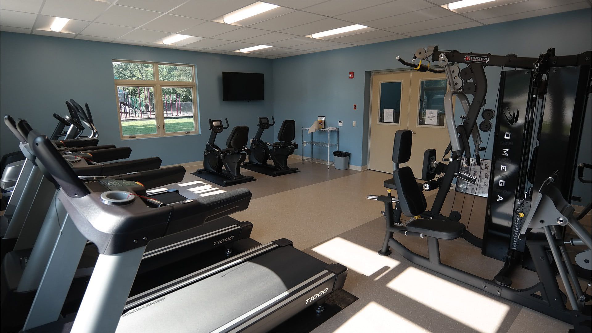 An indoor gym with multiple treadmills, stationary bikes, and a multi-station weight machine in a room with blue walls.