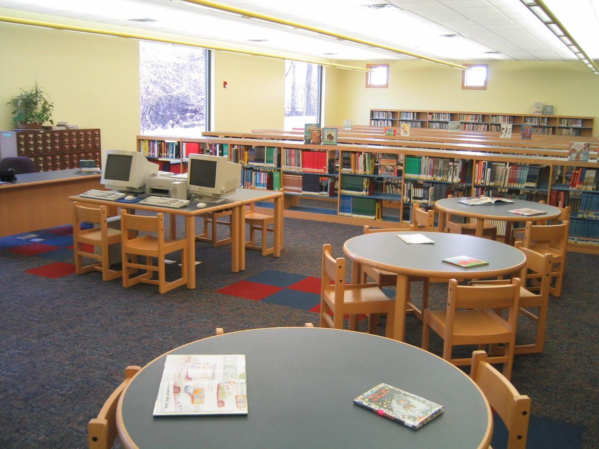 A quiet, empty library featuring round tables, wood chairs, computer workstations, and rows of bookshelves.
