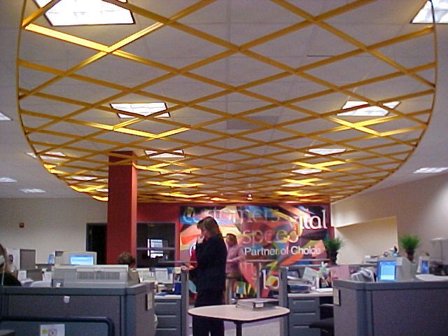 Office interior with a grid of yellow lattice beams suspended from the ceiling above cubicles and a central red pillar.