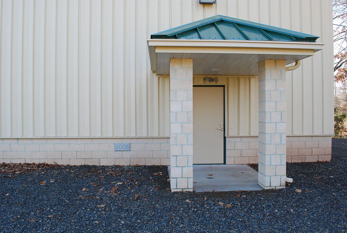 An exterior view of a beige industrial building with a small entryway protected by a green metal awning and stone columns.