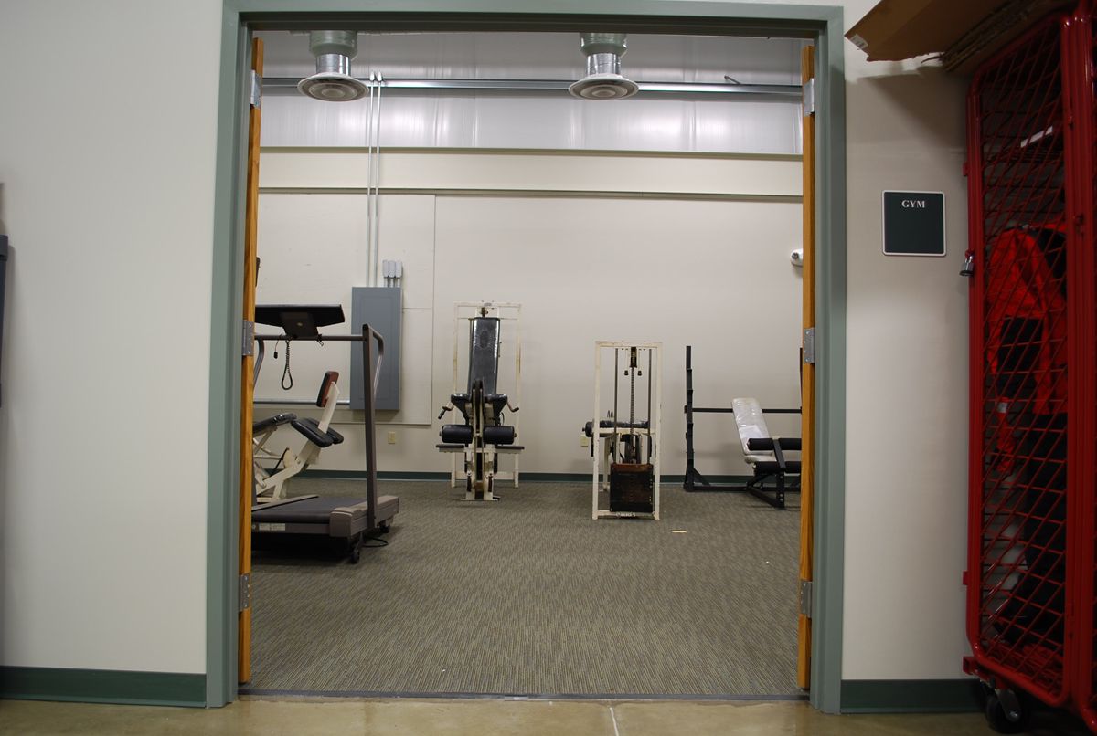 A view through an open doorway into a small, carpeted gym featuring a treadmill and various weight-training machines.