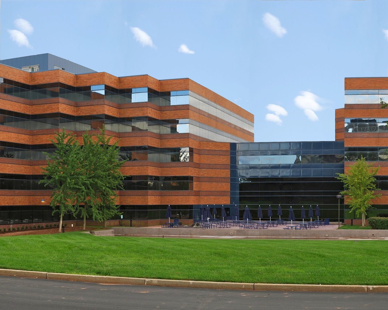 A modern red brick office building with dark windows and a central glass entrance lobby set behind a manicured green lawn.