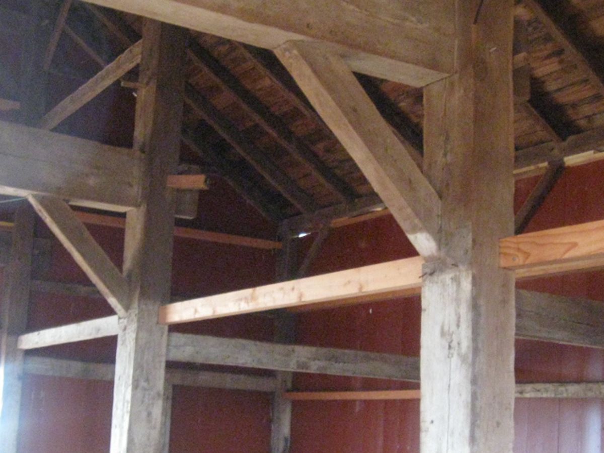 The interior of a barn featuring timber-framed walls with heavy wood posts, diagonal corner braces, and exposed rafters.