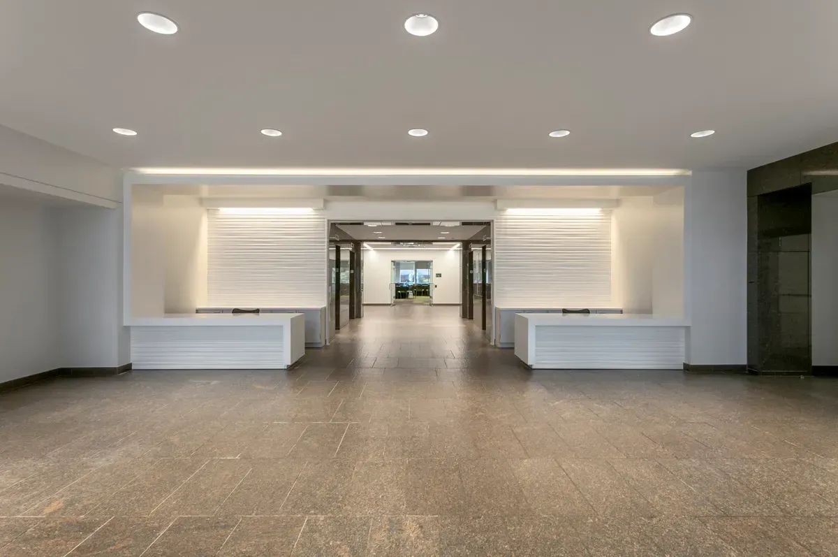 A bright, spacious modern building lobby featuring dual reception desks, stone flooring, and recessed ceiling lighting.