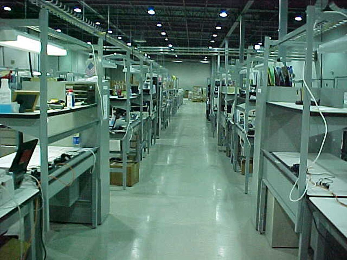 A curved, translucent panel canopy supported by a red steel frame, adjacent to a building with red grid window frames.