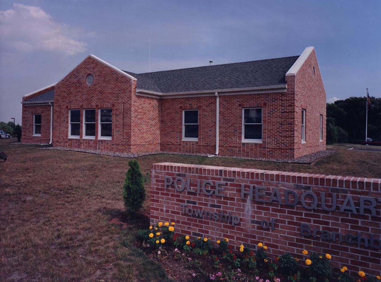 A red brick police headquarters building with a matching brick sign in the foreground, set against a partly cloudy sky.