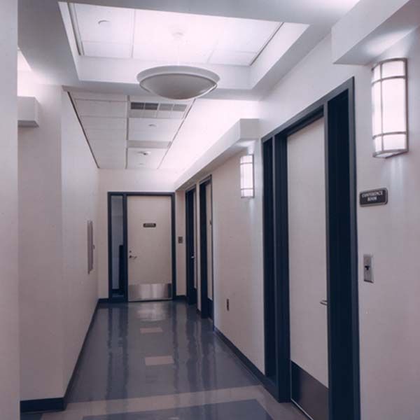 A hallway in a sterile office or medical facility with white walls, gray tiled floors, and multiple closed doors.
