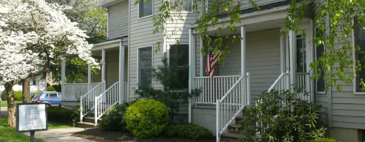 A two-story gray building with porches and white railings, surrounded by trees and a blooming dogwood tree.