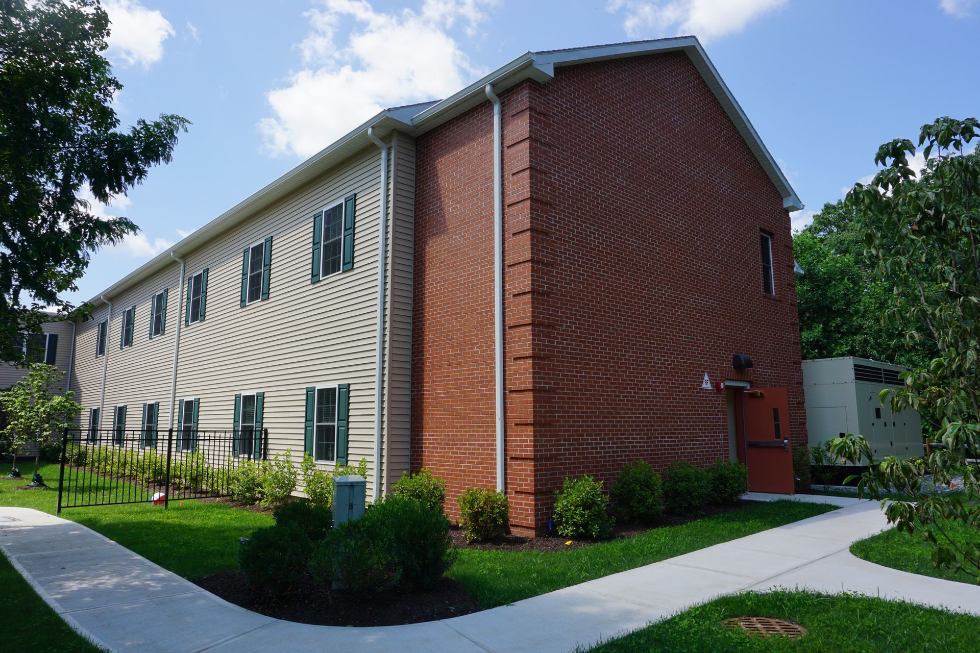 A two-story brick and siding apartment building with green shutters, surrounded by grass and paved walkways.