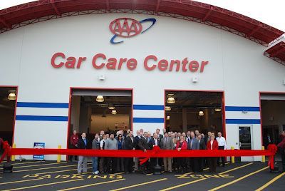 A group of people standing behind a large red ribbon for a ribbon-cutting ceremony at a AAA Car Care Center.
