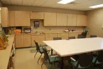 A light-colored, functional meeting room with a large white table, surrounding chairs, and wood cabinetry along the walls.