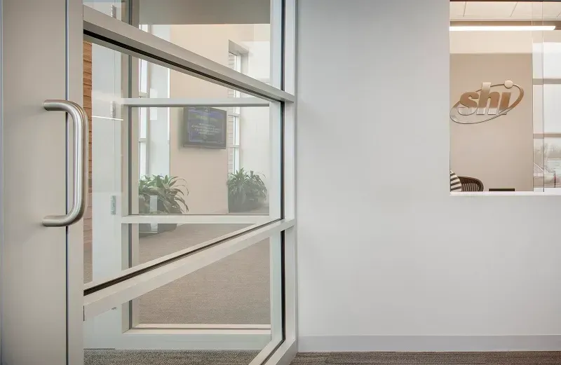 A modern glass door with a silver handle, opening into a bright office interior with a company logo on the wall.