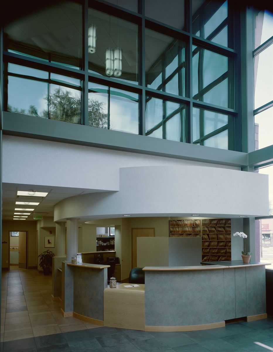 A modern reception desk in a bright, high-ceilinged building with large glass windows and tiled floors.