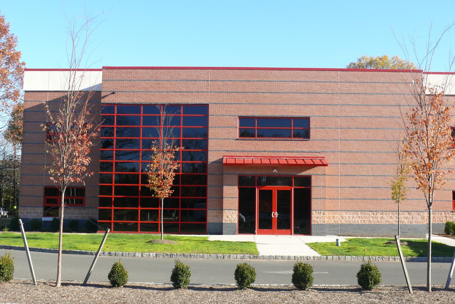A modern, low-rise brick commercial building with a large grid-pattern glass window, red trim, and a centered entrance.