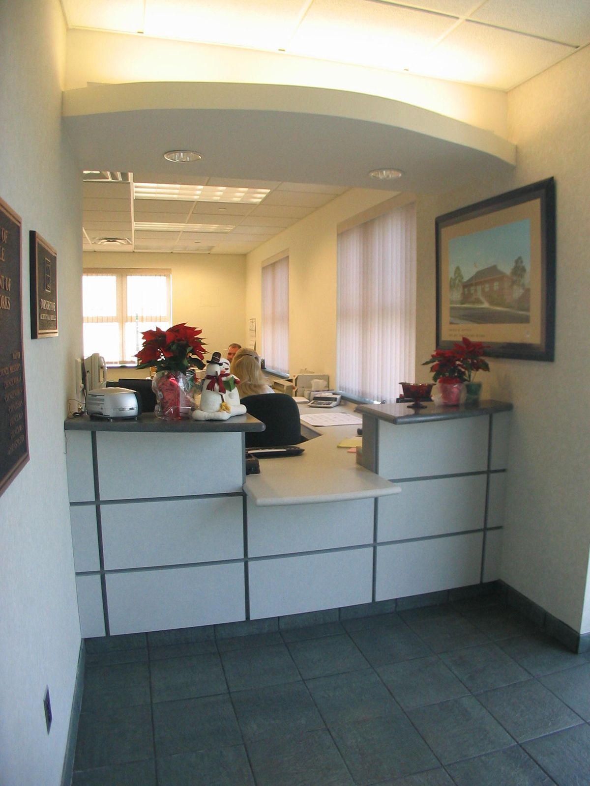 A reception desk in a brightly lit office, featuring white paneling, a desk surface, and decorative poinsettias.