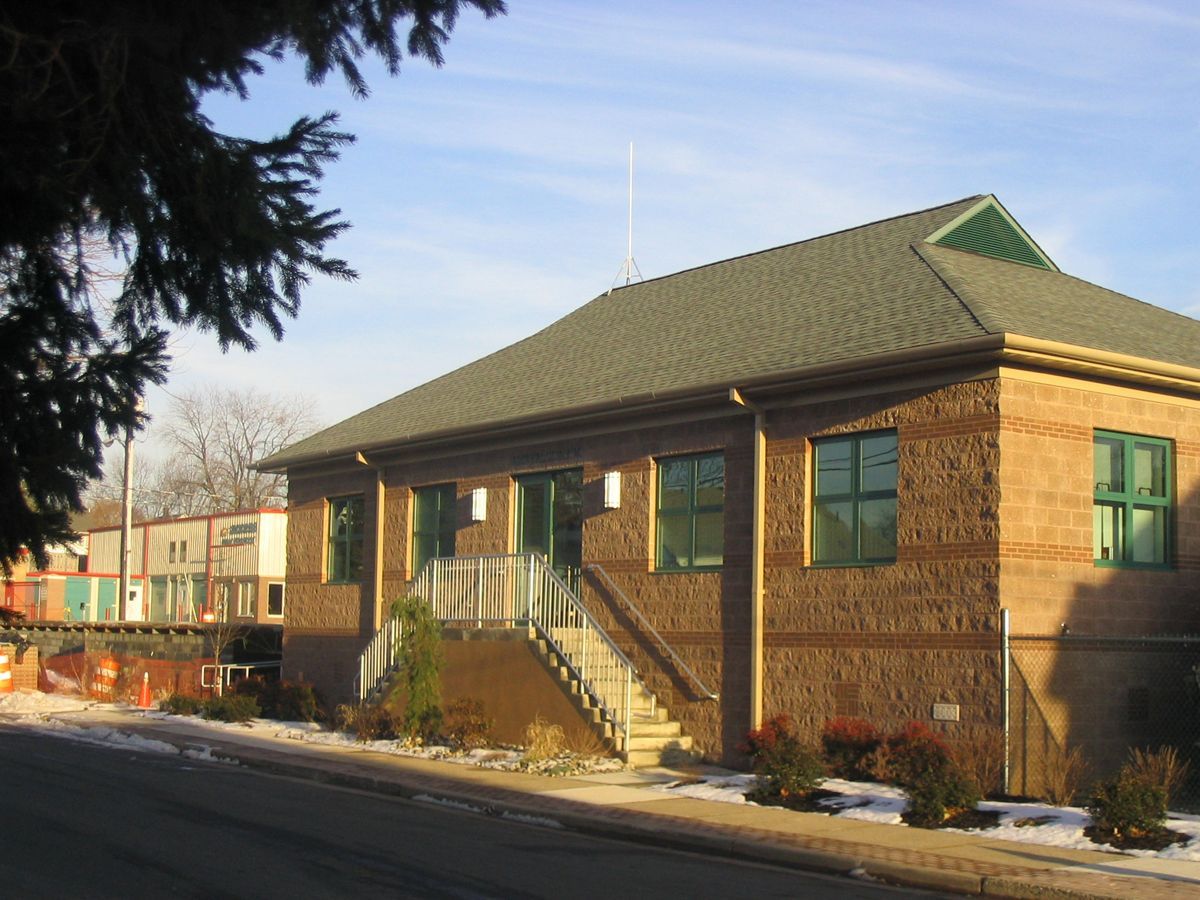 A brick building with a green-trimmed roof and windows, featuring an elevated entrance accessed by a set of stairs.