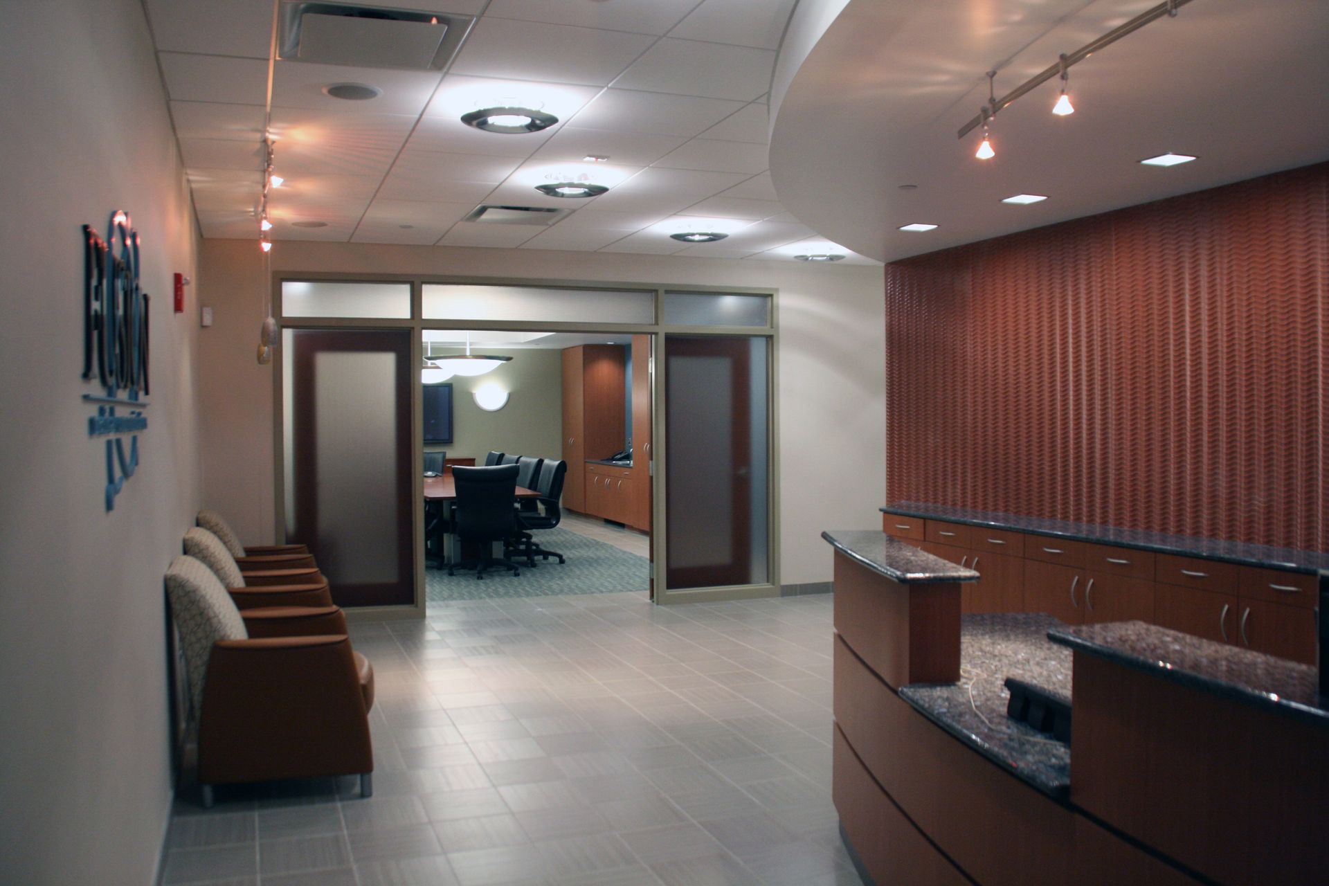 A gym with fitness equipment, treadmills, blue mat squares on a tan floor, and square overhead lights.