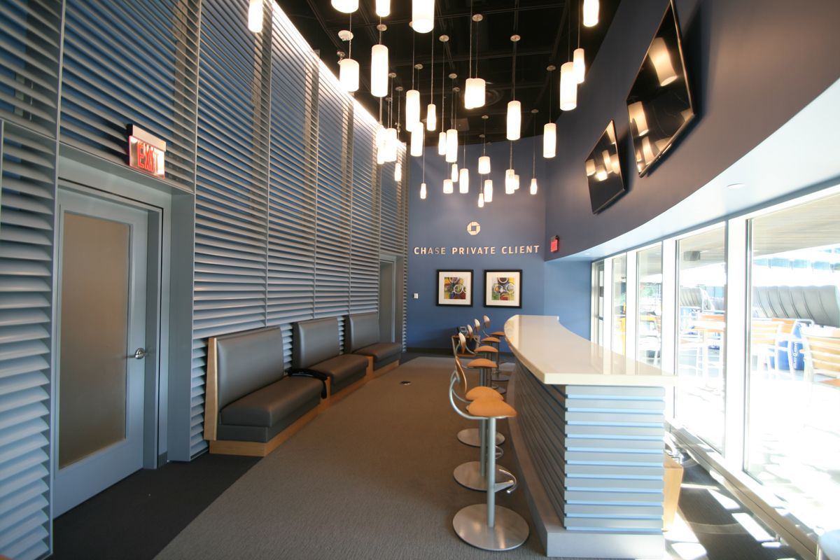 A modern lounge area with gray banquet seating, a bar with high stools, blue walls, and multiple hanging pendant lights.