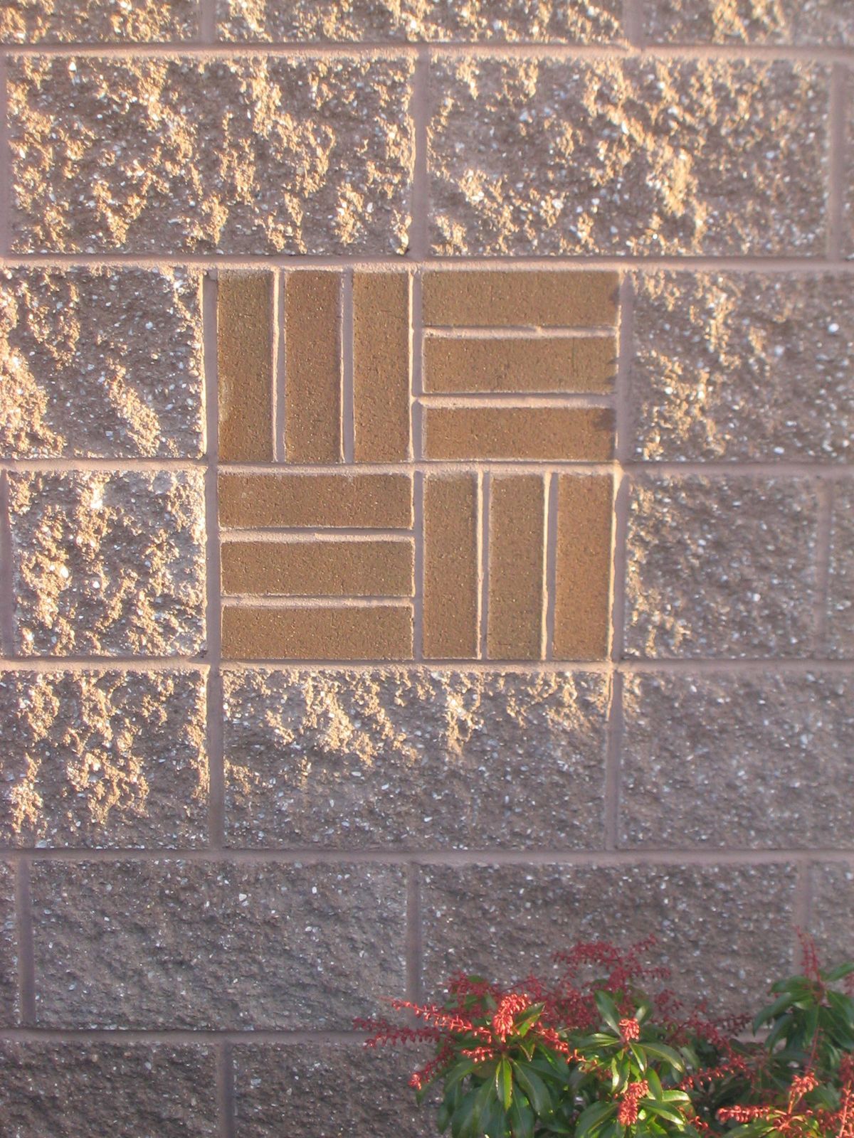 A decorative square inlay of brown bricks in a basketweave pattern, centered on a textured, grey concrete block wall.