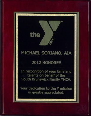 A maroon wooden plaque featuring the YMCA logo, honoring Michael Soriano, AIA, for his service in 2012.