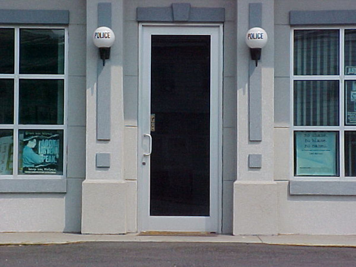 A police station entrance with a dark glass door flanked by two