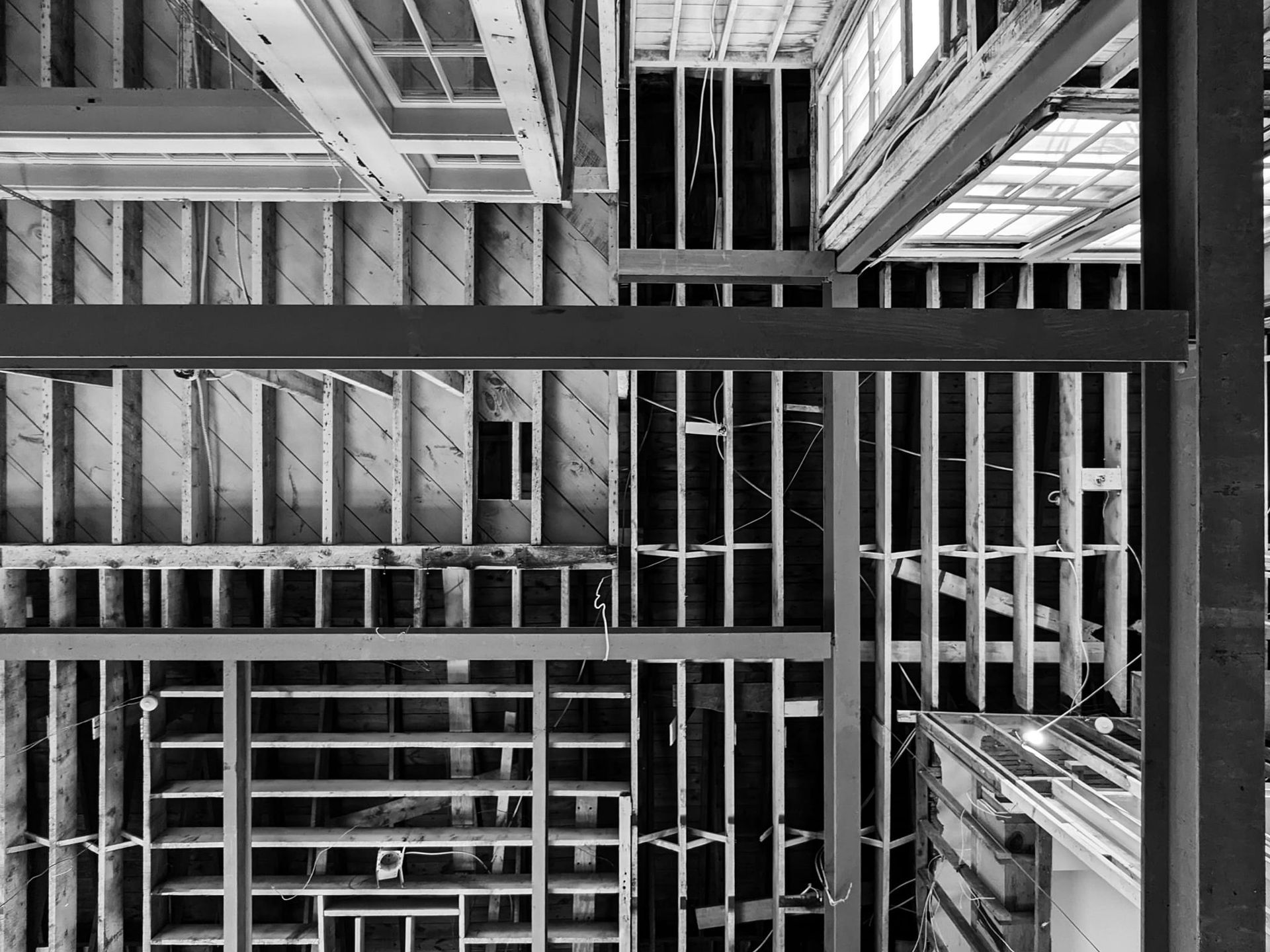 A black-and-white view looking down at the wooden framing and exposed steel beams of a building under construction.