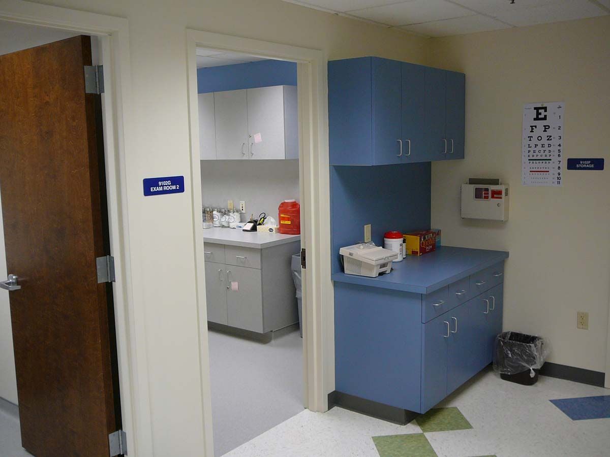 A medical office interior featuring a brown door, an open doorway to a lab area, blue cabinets, and a wall eye chart.