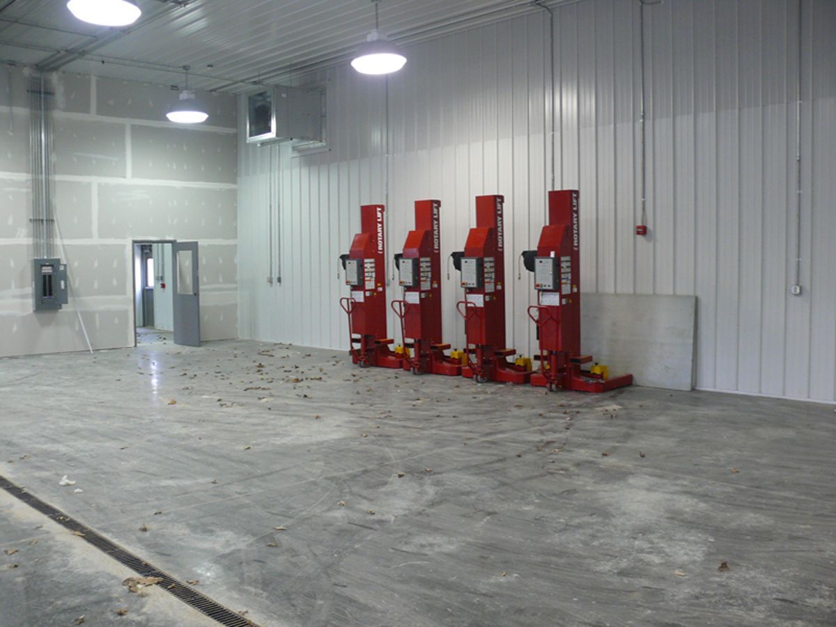 Four red mobile vehicle lifts are lined up against a white wall in a spacious, industrial warehouse with concrete floors.