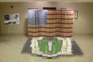 A display made of soda cans featuring a large American flag wall and a floor-level mosaic of the presidential seal.