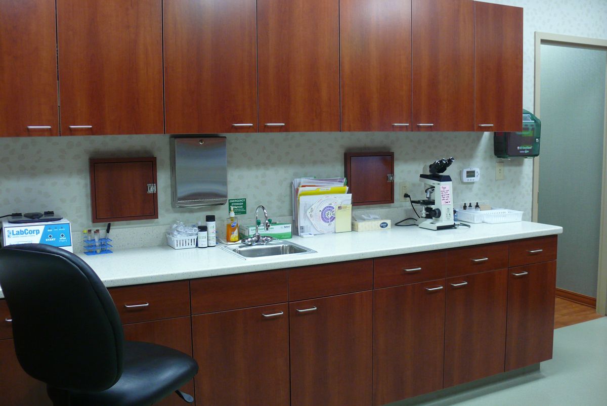 A lab workstation with wooden cabinets, white countertops, a sink, a microscope, and a black office chair.