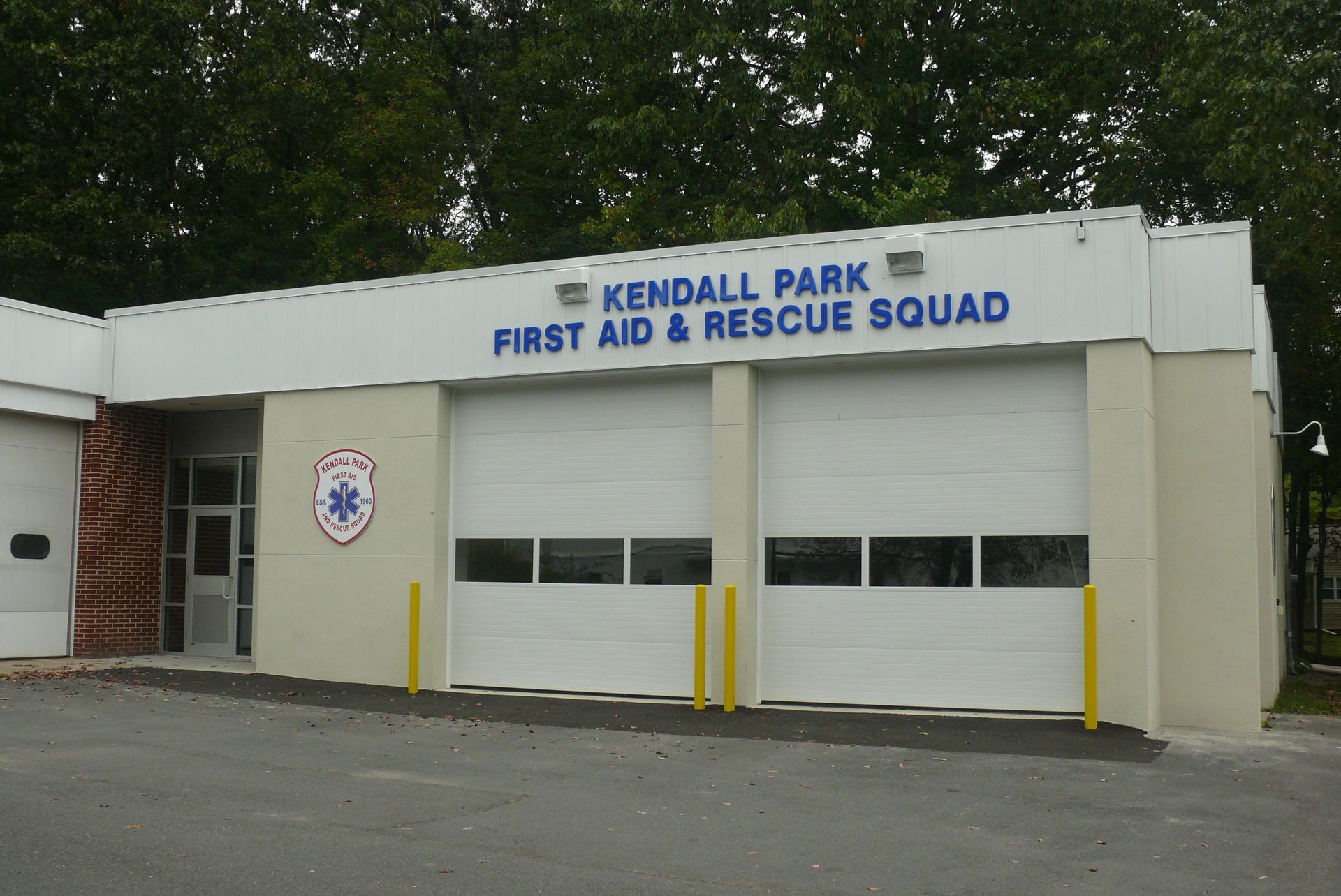 A Kendall Park First Aid & Rescue Squad building with white walls, two garage doors, and an ambulance symbol on the side.