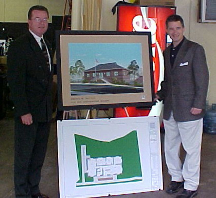 Two people in suits stand beside an easel displaying an architectural rendering of a building and its floor plan.