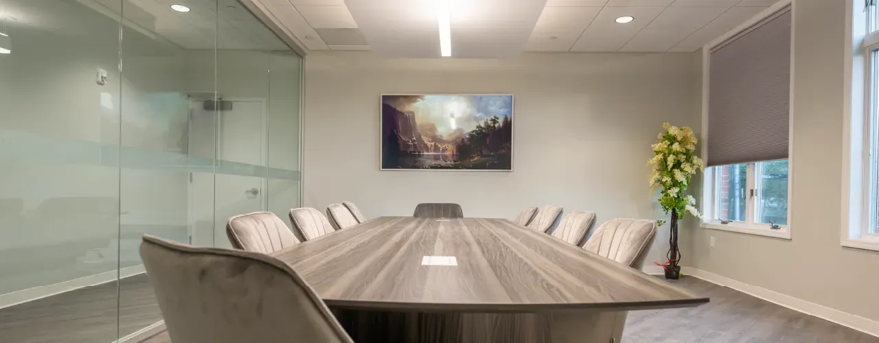 A modern conference room with a long wooden table, plush chairs, glass wall partitions, and a landscape wall painting.