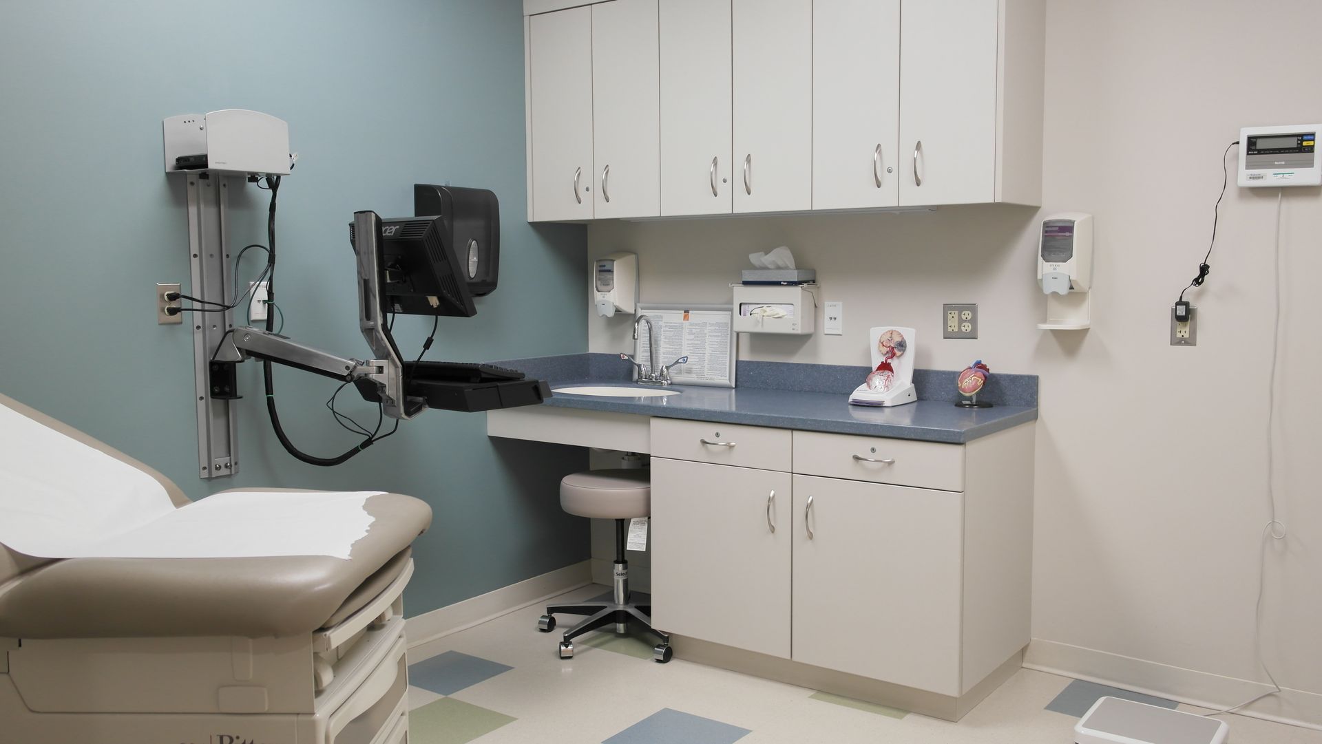 A long, empty indoor hallway with gray carpet, lime green walls in the foreground, and bright overhead lighting.