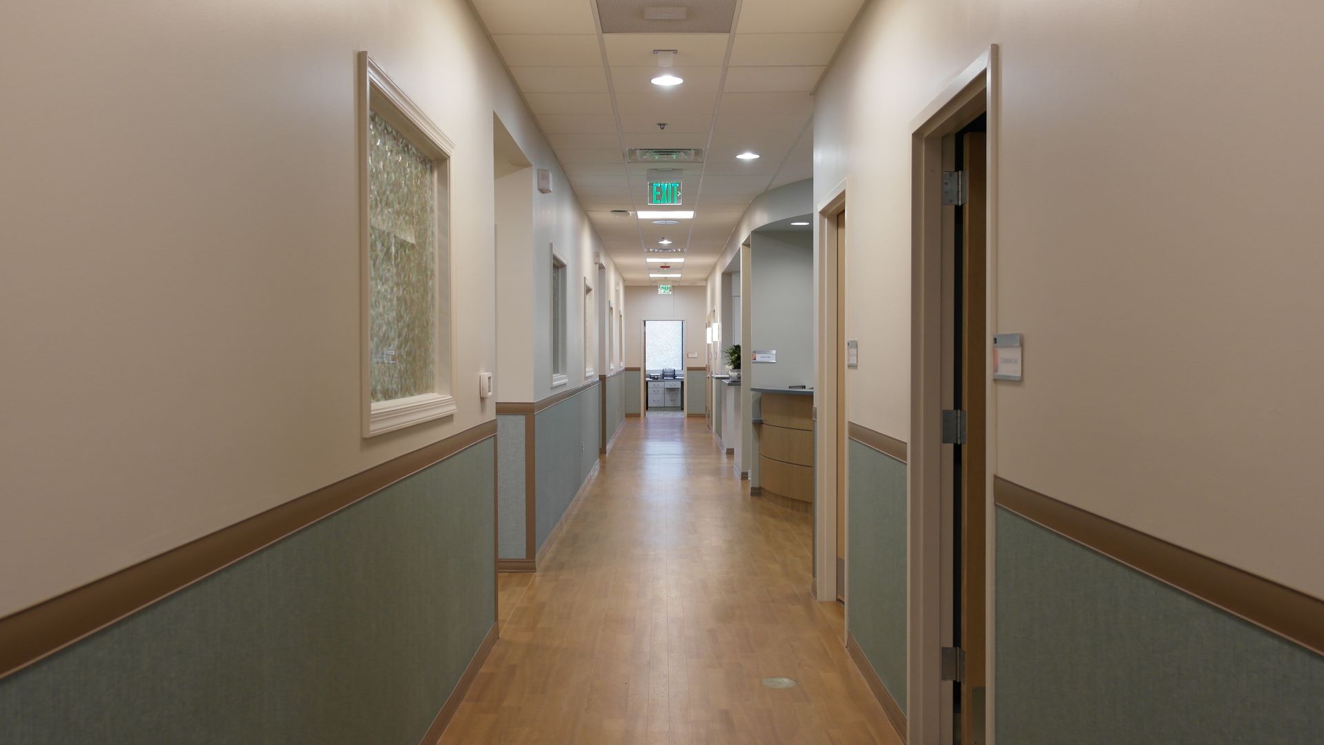 A gym with fitness equipment, treadmills, blue mat squares on a tan floor, and square overhead lights.