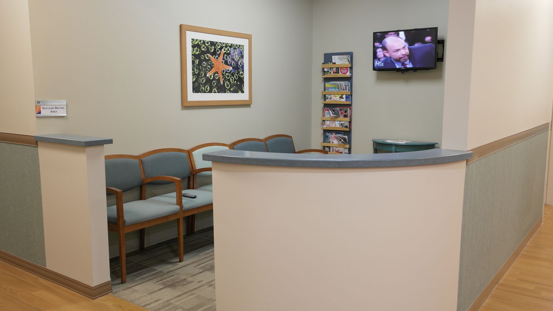 A modern office cubicle with a desk and chair next to a glass wall looking into a warehouse with yellow guardrails.