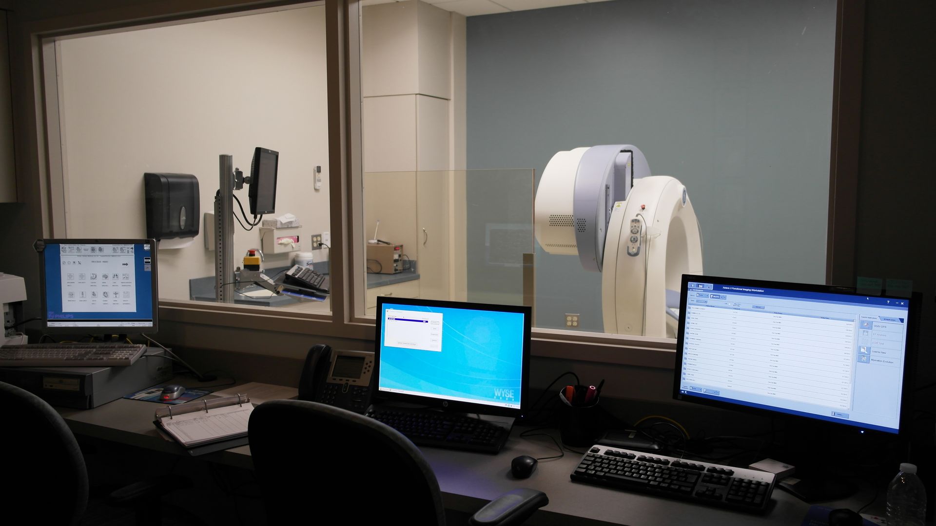 A bright, modern office space featuring rows of grey cubicles with white chairs on a patterned, multi-colored carpet.