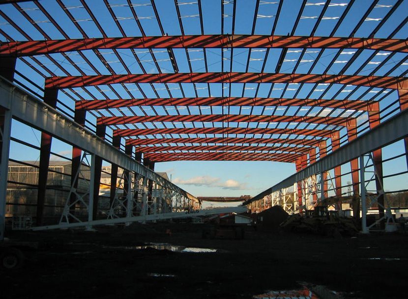 Steel frame of an industrial building under construction against a clear blue sky.