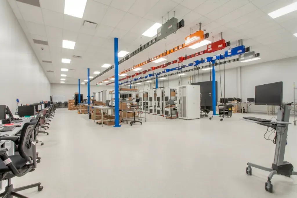 Wide shot of a bright, open-plan laboratory with rows of computer workstations and server racks under ceiling trusses.