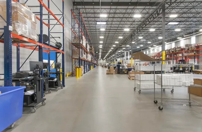 Wide view of an industrial warehouse aisle lined with tall orange-and-blue metal shelving racks and rolling carts.